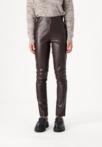 Pantalons en simili cuir marron avec une taille haute, une coupe ajustée et une texture lisse. Associés à des mocassins à plateforme noirs.