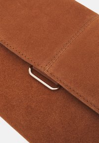 Brun nubuck clutch med en glat tekstur, der har en sølvmetalisk hardware-løkke og præcise sømme langs kanterne.