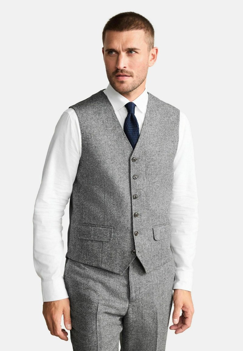 Gray wool blend vest with a notched collar, two front pockets, and button closure. Paired with a white shirt and dark tie. Tailored fit.