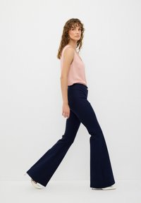 Rosa ärmlös topp och marinblå utsvängda byxor, slät tyg, åtsittande midja, med diskreta sidofickor och vita klackar, modell går framför en neutral bakgrund.