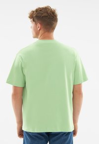 Jasnozielona bawełniana koszulka z okrągłym dekoltem, krótkimi rękawami i luźnym krojem, widok z tyłu. Miękka tekstura i minimum detali.