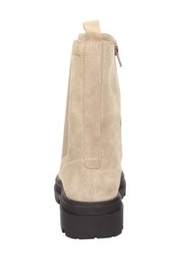 Beige Wildleder-Stiefelette mit schwarzer, robuster Sohle, Reißverschluss hinten und Ziehschlaufe auf weißem Hintergrund, von hinten gezeigt.
