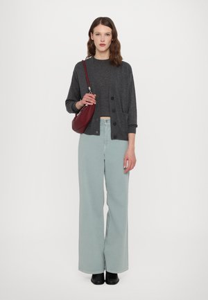 Cardigan grigio sopra un top scuro, abbinato a jeans a gamba larga verde chiaro. Tiene una borsa bordeaux. Scarpe nere completano l'outfit.