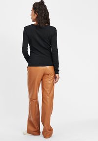 Donker langmouwshirt gecombineerd met glanzende, tan neplederen wijde broek. Het shirt heeft een ronde halslijn en een strakke pasvorm.