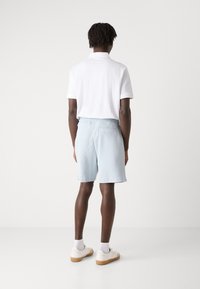 Light blue woven shorts with an elastic waistband, styled for comfort. Paired with a white polo shirt and white sneakers.