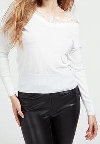 Maglione bianco con dettaglio in pizzo sul colletto, maniche lunghe e orlo a costine, abbinato a pantaloni in pelle nera. Texture liscia, vestibilità casual.