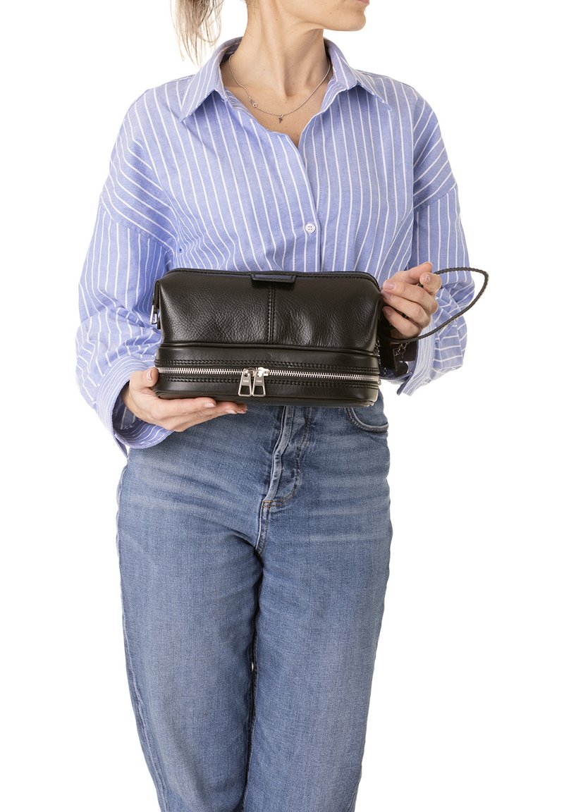 Borsa a mano in pelle nera con forma rettangolare, superficie texture, doppie cerniere e tracolla staccabile. Tenuta da una persona che indossa una camicia a righe.