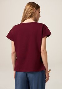T-shirt bordeaux avec une coupe décontractée, des manches courtes retroussées et un col rond. Matière cotonneuse douce avec une texture lisse.