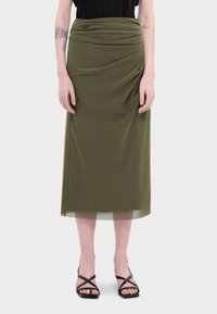 Olivevihreä midi-hame, jossa on draperausyksityiskohtia, pehmeä kangas ja sileä pinta. Yhdistetty mustiin narusandaaleihin.