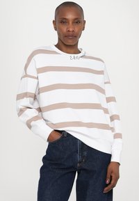 Hvit genser med beige horisontale striper, med rund hals, lange ermer og en avslappet passform. Minimalistisk brodert detalj ved halsen.