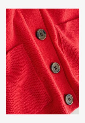 Sarkans adīts kardigans ar divām lielām pogām un apakšējo kabatu. Audums ir mīksts ar ribotām malām.