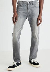 Jean en denim gris avec une coupe droite, design à cinq poches, coutures surpiquées et décoloration subtile ; assorti à des baskets noires et blanches.