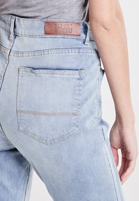 Svijetloplave traperice s visokim strukom, s kožnom oznakom "Urban Classics" i stražnjim džepom sa šivanim šavom.
