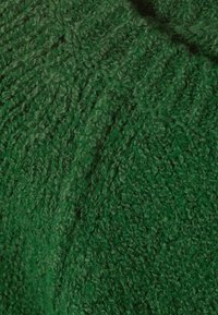 Close-up van dikke, groene gebreide stof met gedetailleerde kabels en textuurvezels van wol.