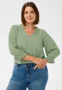 Hellgrüne Bluse mit strukturierter Oberfläche, V-Ausschnitt und Volantbesatz; verfügt über lange, geraffte Ärmel und eine entspannte Passform.