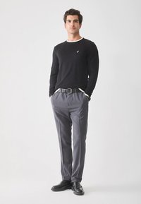 Czarny sweter z długim rękawem z białym kołnierzykiem, szare dopasowane spodnie, czarny pasek i błyszczące czarne buty. Model stoi prosto.