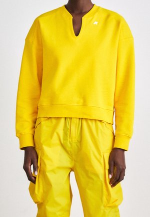 Person iført en knaldgul langærmet top med en notch-halsudskæring og matchende cargobukser med sidelommer.