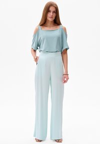 Lichtblauwe off-shoulder blouse met borduursel op de banden, gecombineerd met luchtige, hoge taille palazzobroek in dezelfde kleur. Vlotte textuur.