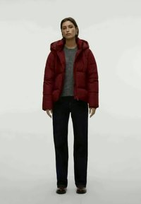 Punane puhvikjakk kapuutsiga, tepitud tekstuuriga, lukuga, kantud halli sviitri peal, kaasas tumedad püksid ja mustad kingad.