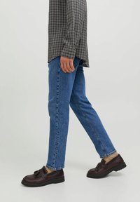 Jeans de mezclilla azul con corte recto, combinados con mocasines marrón oscuro que tienen un lazo como acento. El conjunto incluye una camisa de cuadros.