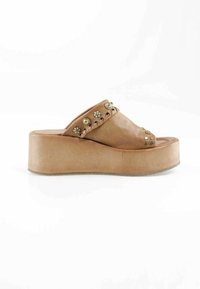 Sandale à plateforme beige avec semelle épaisse, décorée de clous métalliques et de rivets floraux sur la sangle supérieure.