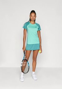 Αθλητική ενδυμασία από ανοιχτό μπλε ύφασμα, που περιλαμβάνει μια εφαρμοστή μπλούζα και μια ταιριαστή φούστα. Μια ρακέτα τένις και μια μπάλα κρατούνται σε ένα χέρι.