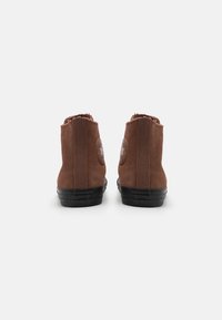 Botoși de gleznă din suede maro cu o finisare texturată, dotati cu o talpă din cauciuc negru și un logo circular pe lateral. Detaliu cu margine franjurată.