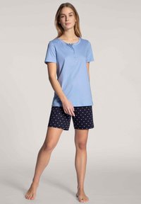 Lichtblauwe katoenen T-shirt met korte mouwen en een drieknops sluiting, gecombineerd met donkerblauwe shorts met kleine witte hartpatronen.