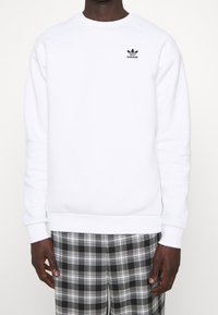 Vitt crewneck-oversize i mjukt tyg, med en liten svart Adidas-logotyp på bröstet samt ribbade muddar och fåll.