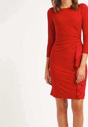 Vrouw draagt een knielange rode jurk met driekwart mouwen en een gerimpelde detail aan de rechterzijde.