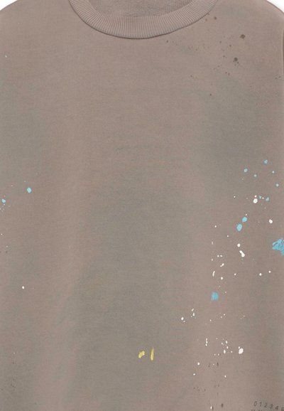 Maglietta girocollo marrone chiaro con piccoli motivi sparsi di schizzi di vernice nei colori blu, bianco, giallo e marrone.