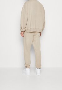 Felpa beige e pantaloni della tuta, tessuto morbido, vestibilità comoda. Sneaker bianche. Design semplice con spalle scese e polsini a costine.
