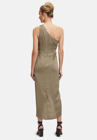 Oliwkowa midi sukienka z jednym ramieniem o dopasowanym kroju. Posiada zamek błyskawiczny z tyłu oraz gładką, czystą fakturę. Widać obcasy.