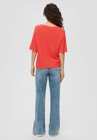 Korallenfarbenes, oversized Strickoberteil mit kurzen Ärmeln, kombiniert mit hellblauen, hochgeschnittenen Schlagjeans. Gerippte Struktur und entspannter Schnitt.
