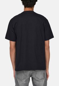 Schwarzes Baumwoll-T-Shirt mit lockerer Passform, kurzen Ärmeln und Rundhalsausschnitt, von hinten präsentiert.