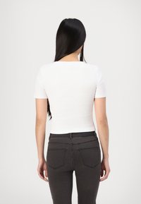 Top corto bianco a maniche corte con design aderente, abbinato a jeans neri con tasche posteriori e vita media.