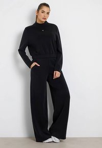 Completo sportivo nero composto da una maglia a maniche lunghe con scollo rotondo e pantaloni a gamba larga a vita alta, realizzati in tessuto liscio e morbido.