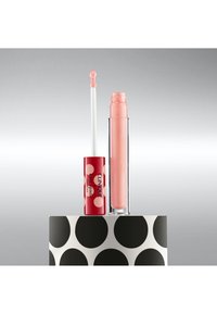 Lipgloss in een doorzichtige perzikkleurige tube met een rode, met stippen bedekte dop. Inclusief een flexibele applicator met een afgeronde punt.