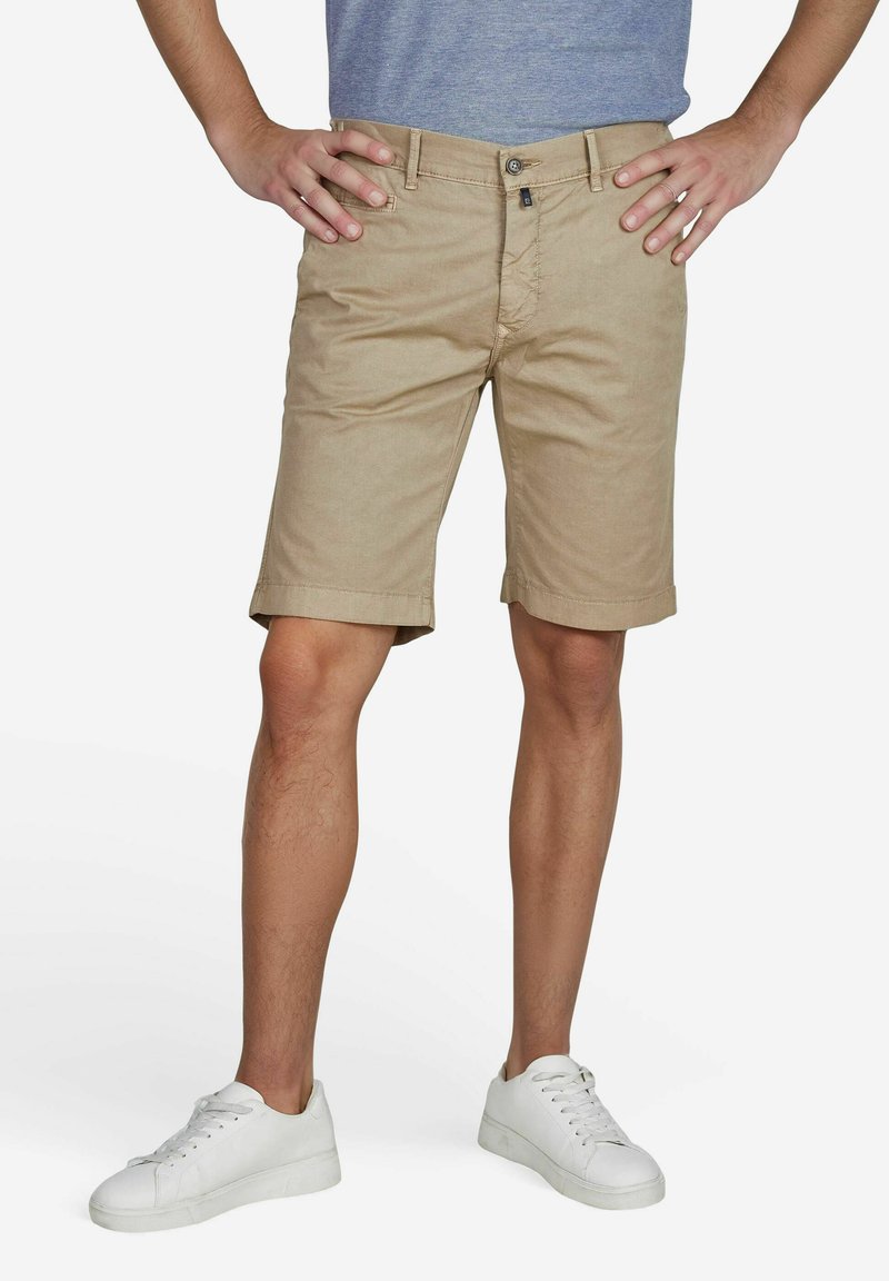 Khaki shorts met een rechte pasvorm, opgerolde zoom, sluiting met een knoop aan de voorkant en riemlussen, gecombineerd met witte sneakers. Katoenen stoftextuur.