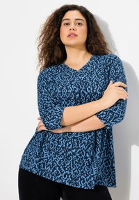 Modrý a černý top s vzorem, výstřihem do V a třičtvrtinovými rukávy. Měkká, texturovaná látka s asymetrickým lemem.