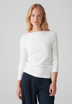 Weißes Ripp-Longsleeve mit einem Bootsausschnitt, ausgestattet mit einem figurbetonten Design und glatter Textur, kombiniert mit dunkelblauen Hosen.