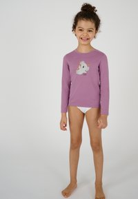 Maglietta a maniche lunghe di lavanda con una grafica grigia di un koala. Il bambino indossa pantaloni corti bianchi sotto, in piedi scalzo su uno sfondo neutro.