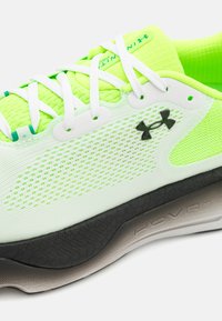 Zapatilla de running de malla verde con cordones blancos y suela negra y gris. Cuenta con una parte superior transpirable, acentos texturizados y un logo prominente.