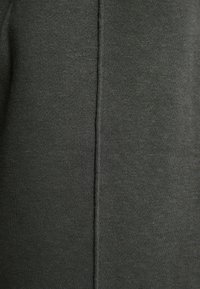 Ciemnozielona tkanina o gładkiej fakturze, z pionowym szwem biegnącym przez środek. Materiał wydaje się lekko elastyczny i przewiewny.