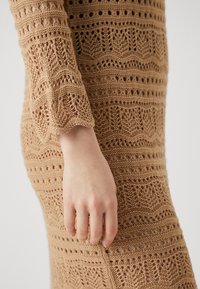 Κεντημένο φόρεμα σε ανοιχτό καφέ χρώμα, με περίπλοκα σχέδια, ανοιχτόχρωμες λεπτομέρειες και σχεδίαση μανικιού με θίγμα.