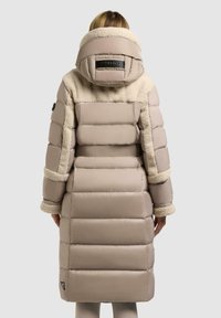 Beige pufferjas met pluche stofaccenten, een grote capuchon en horizontaal gestikte secties. Heeft een logo-embleem op de achterkant en getextureerde manchetten.