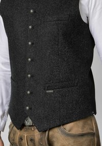 Dunkelgraue Wollweste mit sechs metallischen Knöpfen, einer Brusttasche und einem Rücken aus kontrastierendem Stoff, kombiniert mit beige Lederhosen.