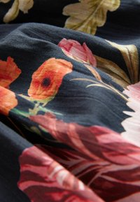 Blommönstrad tyg, med orange och rosa blommor på en mörk bakgrund. Texturen verkar mjuk och något skrynklig.