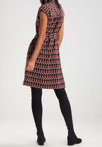 Robe à motifs avec un corsage ajusté, des manches courtes et une ceinture à la taille. Les couleurs comprennent des formes géométriques rouges, noires et blanches.