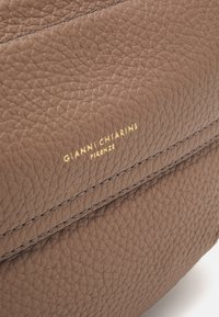 Zbliżenie na teksturowaną brązową torebkę skórzaną z podwójnym przeszyciem i złotym logo "Gianni Chiarini Firenze".